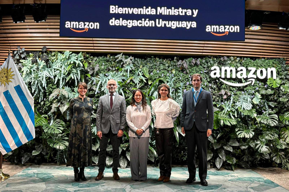 Visita a AWS Cardona y otras personas, junto a bandera uruguaya; detrás, banner de AWS