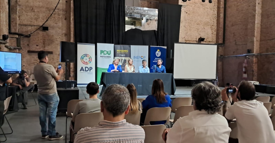Público sentado. De fondo, mesa y banners institucionales