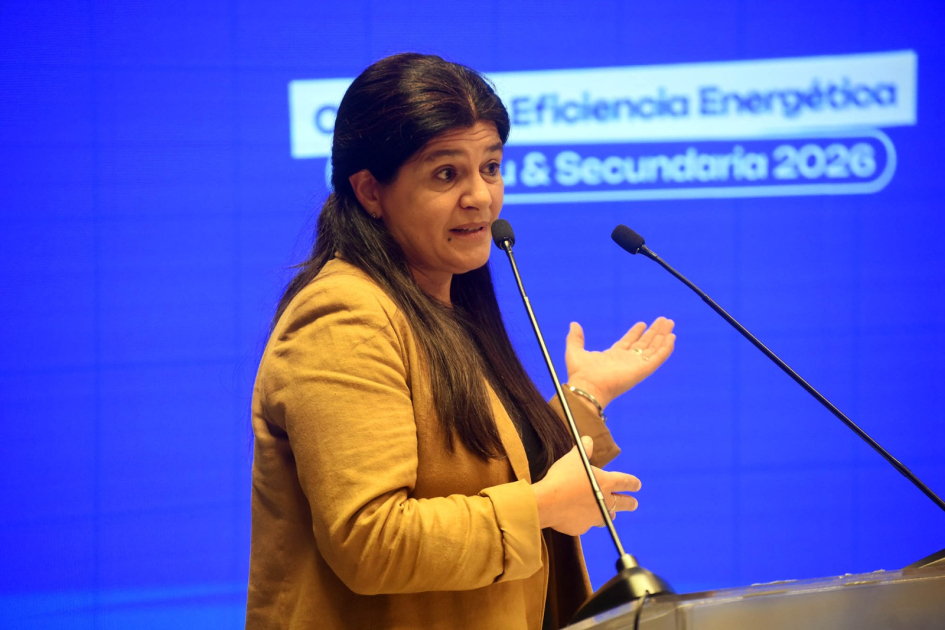 Arianna Spinelli de perfil habla a micrófono. Al fondo, pantalla azul