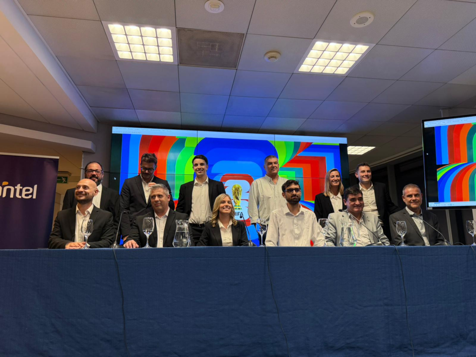 Equipo periodístico Equipo periodístico detrás de mesa con mantel azul. Algunas personas paradas y otras sentadas