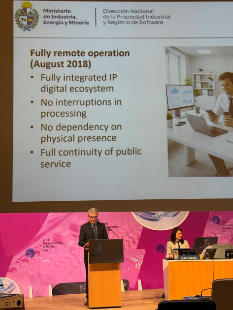 Persona parada detrás de un atril; arriba, pantalla