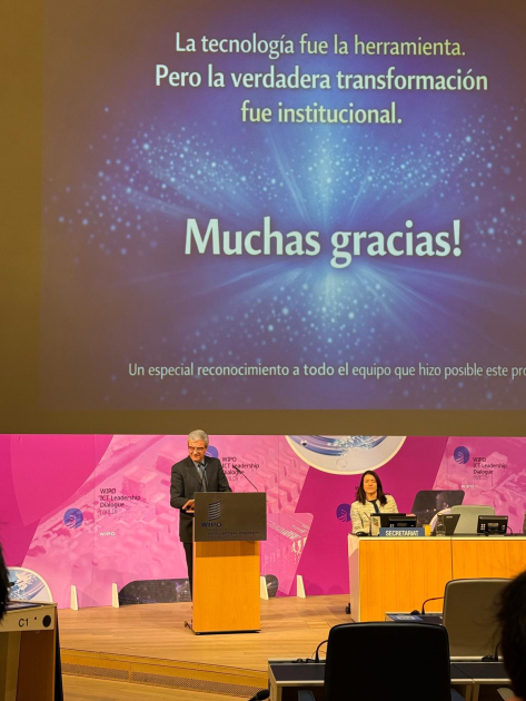 Persona parada detrás de un atril; arriba, pantalla