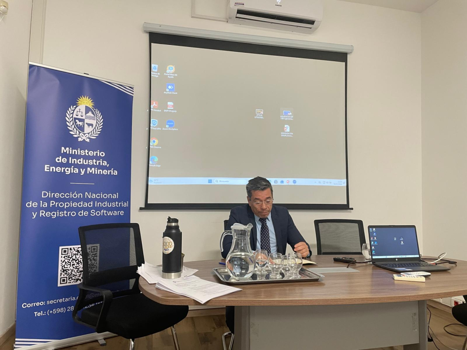 Persona sentada detrás de una mesa con una pantalla detrás