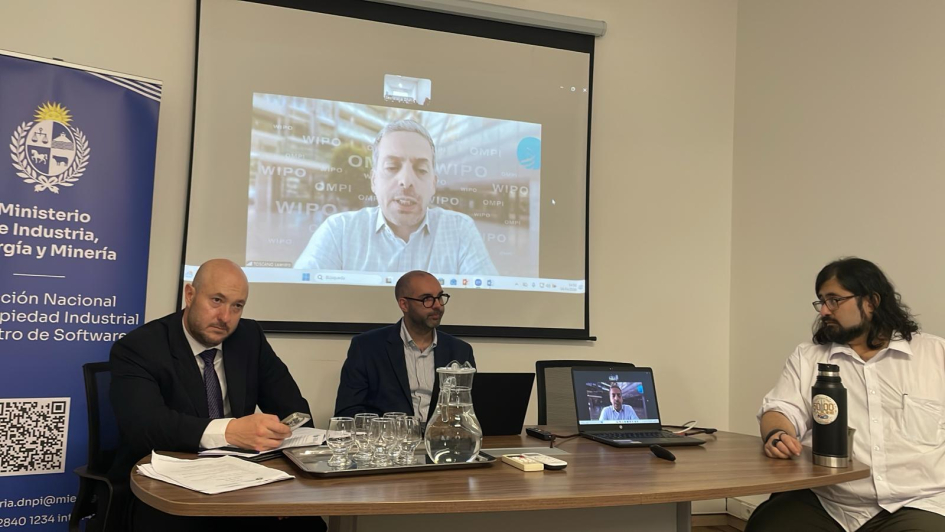 Tres personas sentadas detrás de una mesa y con una pantalla al fondo