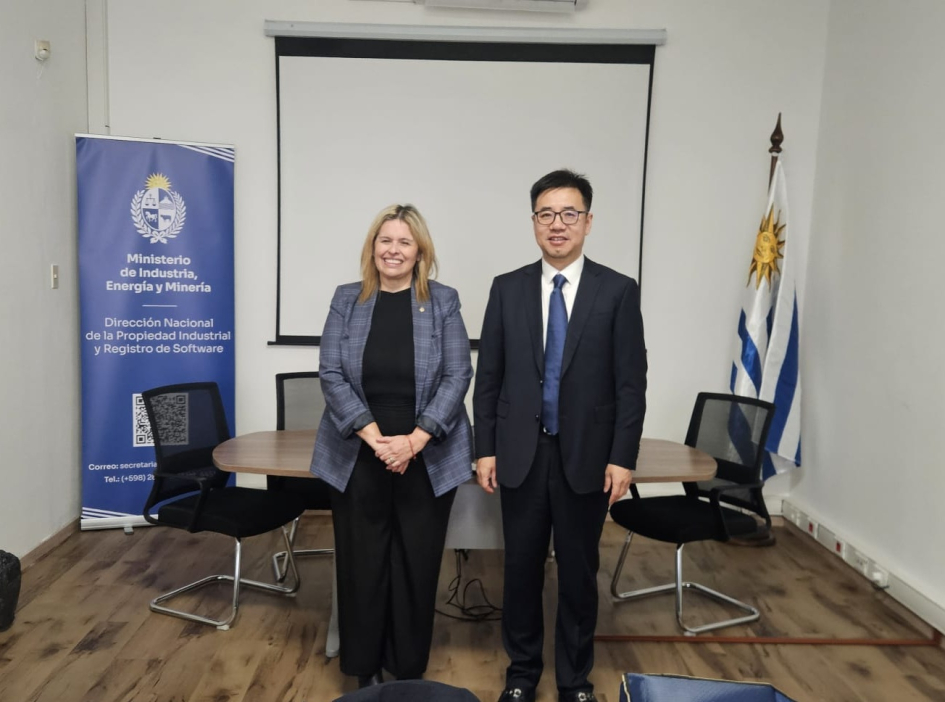 Directora Marianela Delor y comisionado adjunto, Oficina de Patentes, CNIPA, Li Shengjun. Foto: DNPI Dos personas de pie; detrás, banner institucional y bandera uruguaya