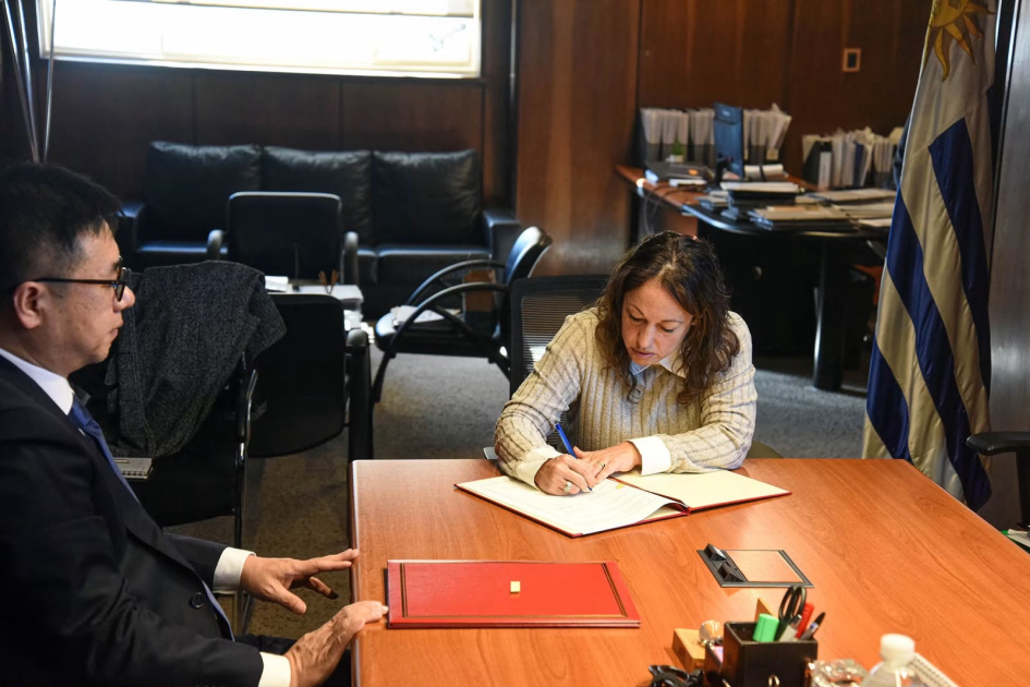 Firma de memorándum de entendimiento entre DNPI y CNIPA. Foto: MIEM. Una persona firma un documento y otra persona está sentada al lado
