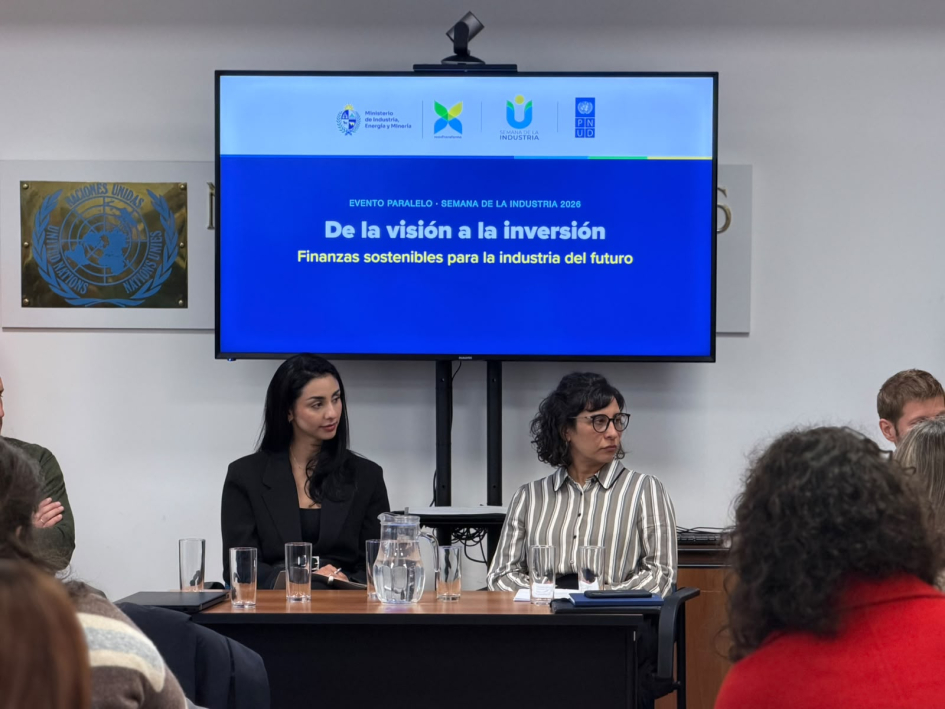 Souza y Balsa, sentadas en una mesa; de espaldas y frente a ellas, públicos; encima, pantalla