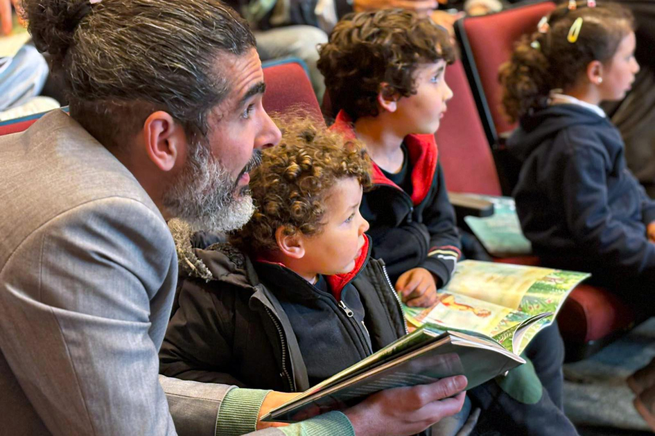 Rodrigo Díaz El director general del MIEM, sentado junto a niños, sostiene un libro en sus manos