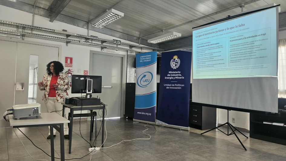 Módulo 1 en Salto: la consultora Silvana Papagno expuso ante las y los participantes Silvina Papagno de pie expone; pantalla y banners institucionales