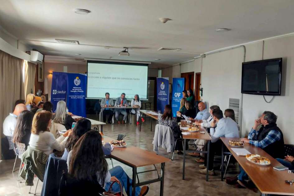 Participantes del encuentro Plano general del taller; personas sentadas en mesa; al fondo, pantalla