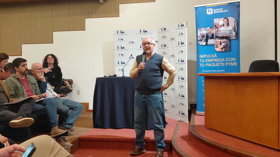 Espacio de intercambio entre instituciones, productores y productoras y empresas. Hombre de pie y personas sentadas