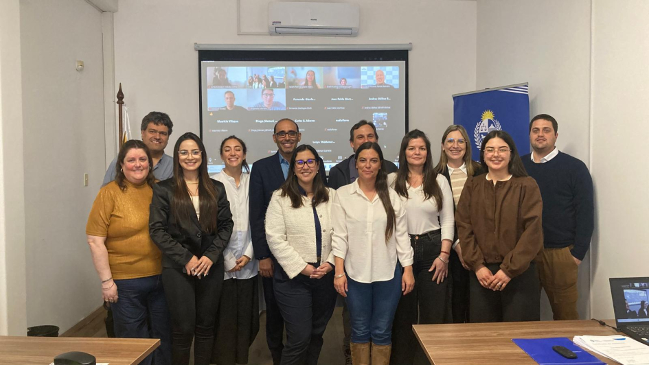 Doce personas paradas, con una pantalla detrás, con la imagen de reunión por Zoom