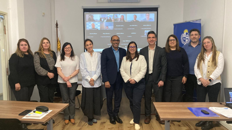 Diez personas paradas con una pantalla detrás, que tiene la imagen de una reunión por Zoom
