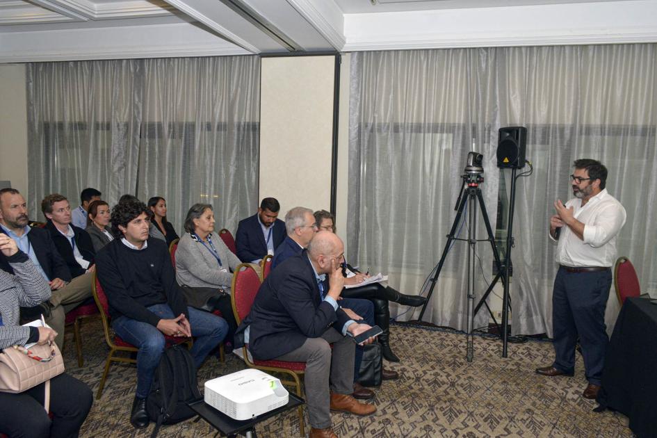 Personas reunidas en una sala; habla, de pie, el director Maciel