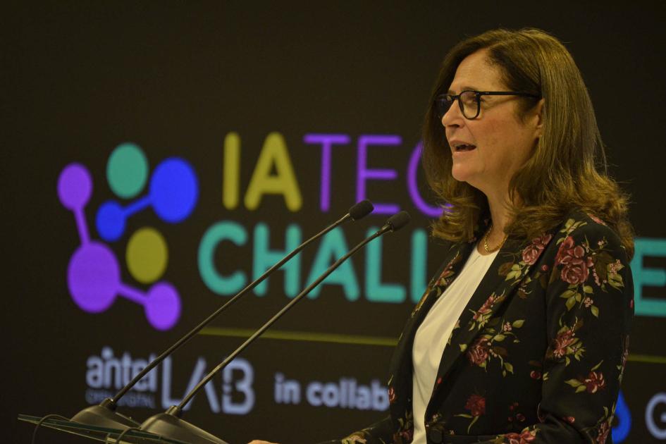 Ministra Elisa Facio Ministra habla con un micrónofo; detrás, logo del evento