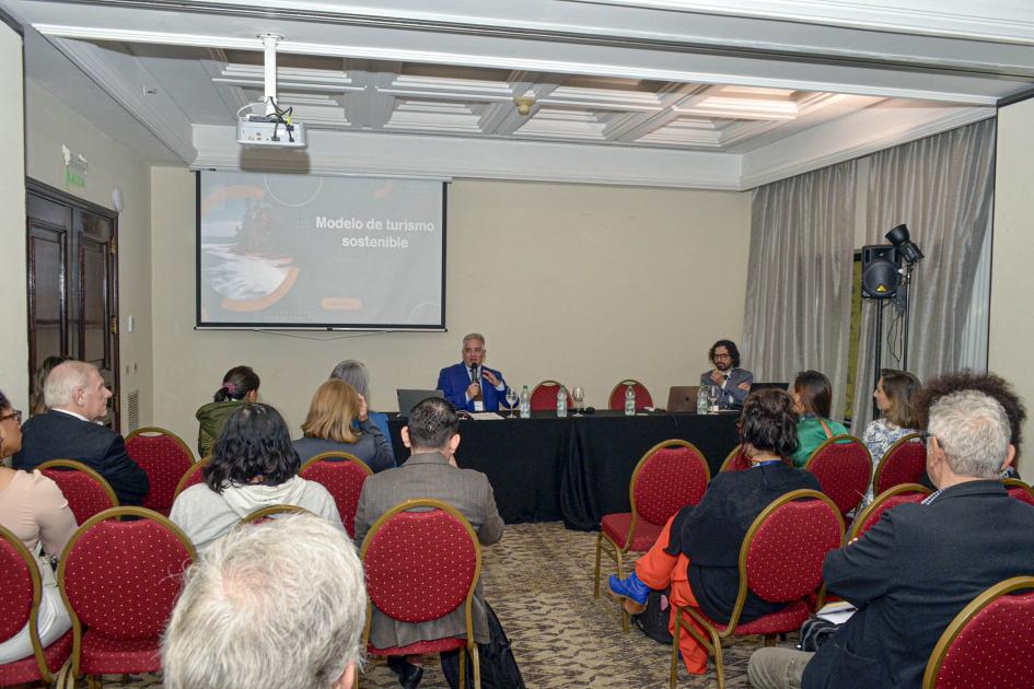 Taller del sector turismo Sala vista desde atrás; al fondo, pantalla y mesa de expositores