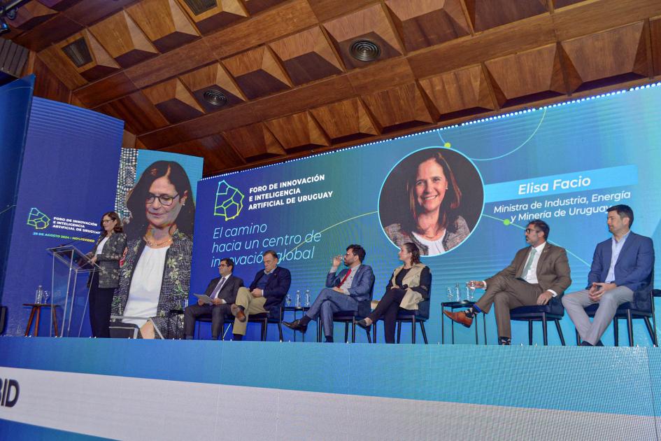 Panel que inauguró la ministra Elisa Facio Escenario: a la izquierda, Facio habla desde un atril; a su lado, expositores; detrás, gran pantalla
