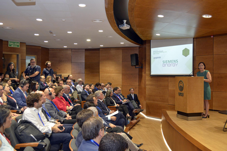 Ministra Cardona habla desde atril. Público sentado. 