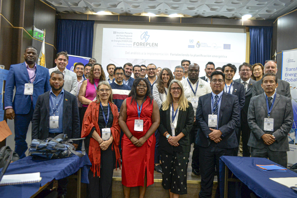 Representantes de la delegación posan de pie en salón; detrás, pantalla