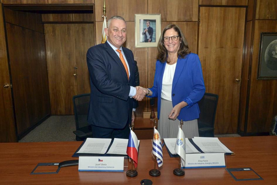Los ministros se saludan luego de la firma del acuerdo Ministra Facio y ministro Sikela se dan la mano; frente a ellos, hay una mesa con los documentos