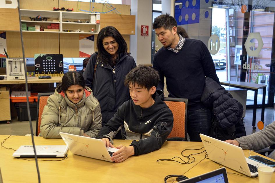 Dos adultos y dos adolescentes miran computadoras en una mesa