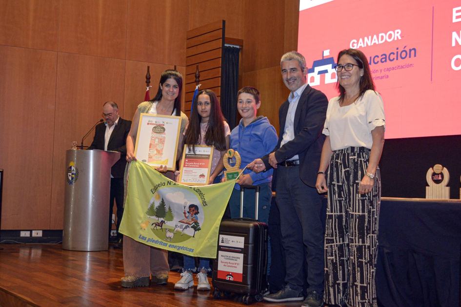 Niñas, niños, docentes y autoridades, reciben el premio; detrás, pantalla