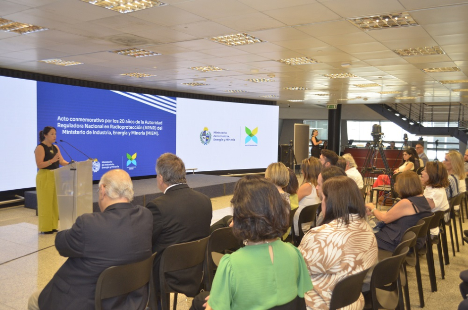 Fernanda Cardona habla. Público sentado Público sentado. Al fondo, Cardona habla de pie. Pantallas con logos institucionales