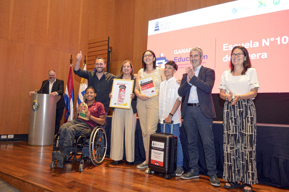 Autoridades, docentes, niñas y niños, de pie (un niño se traslada en silla de ruedas), sobre escenar