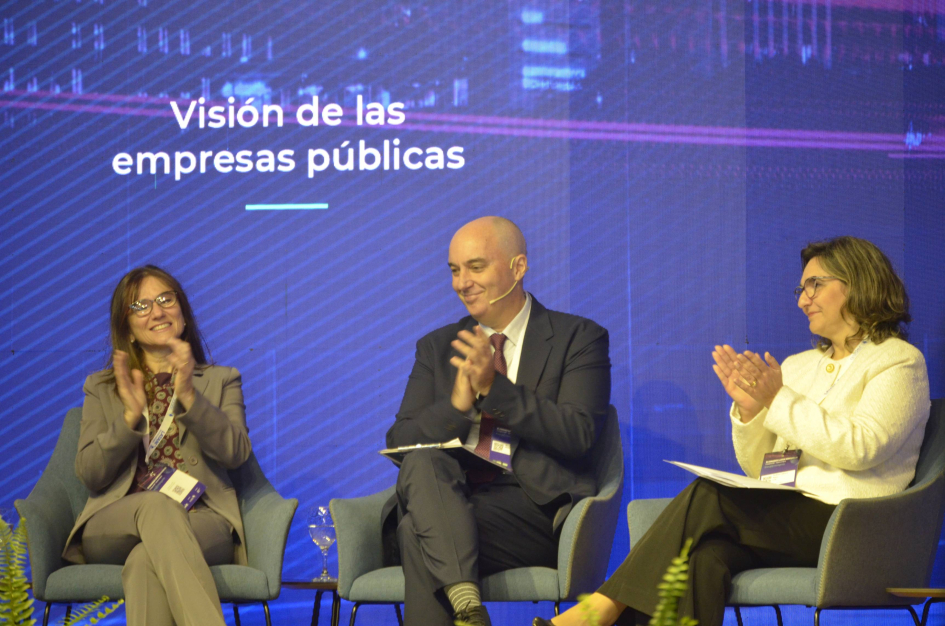 Cecilia San Román, Marcelo Mula y Andrea Cabrera San Román, Mula y Cabrera, sentados, aplauden; detrás, pantalla con nombre del evento