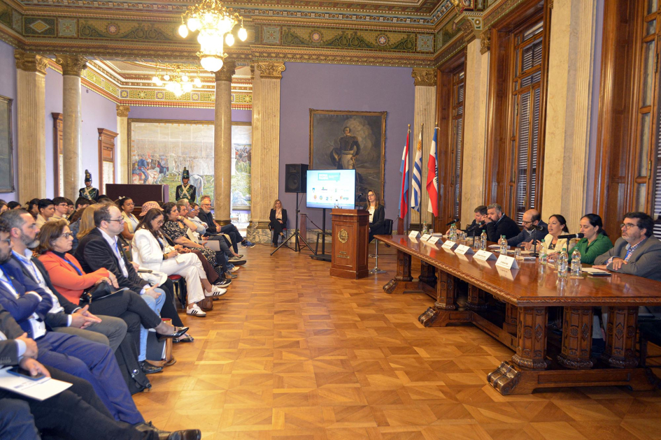 A la derecha, mesa de autoridades; a la izquierda, público, sentado; ambos se ven de perfil