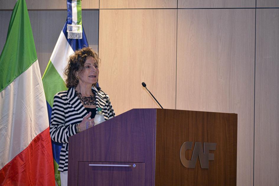 Secretaria general de IILA, Antonella Cavallari Antonella Cavallari habla desde un atril con el logo de CAF; detrás, banderas