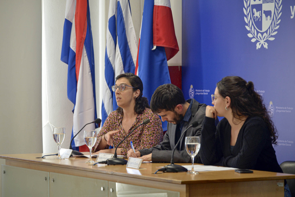 Tres personas, sentadas; detrás, banderas y banner azul