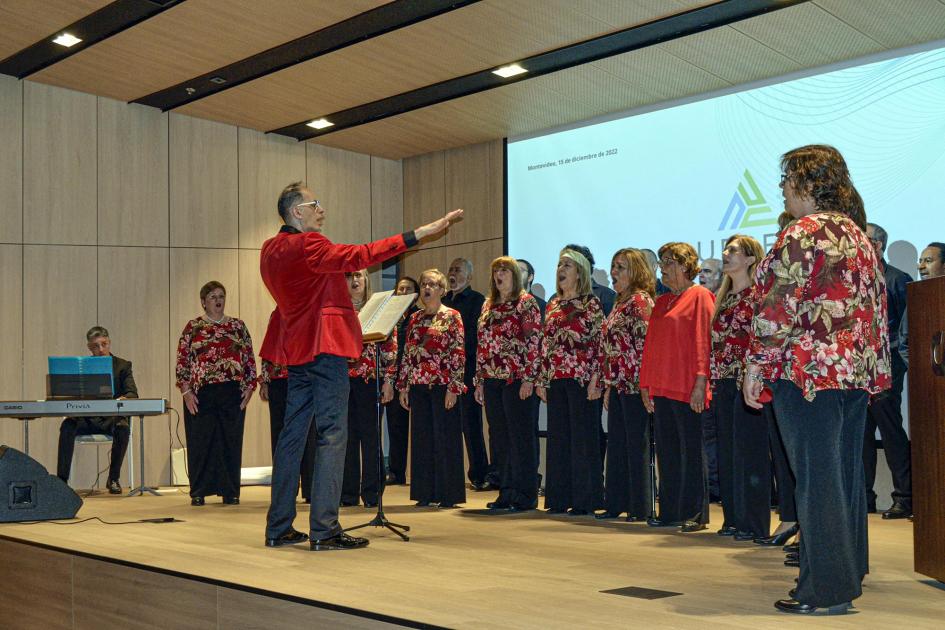 Un coro de mujeres y hombres canta sobre el escenario; detrás hay una gran pantalla