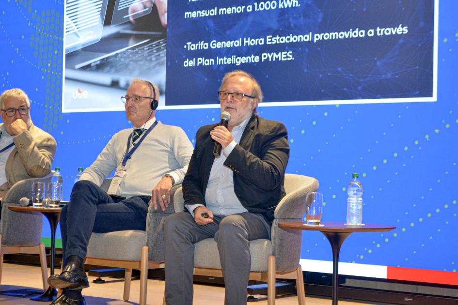 gerente de la División de Estudios y Procesos Comerciales de UTE, Juan Carlos Patrone Patrone habla sentado en un siillón; a su lado, dos hombres; detrás, una gran pantalla