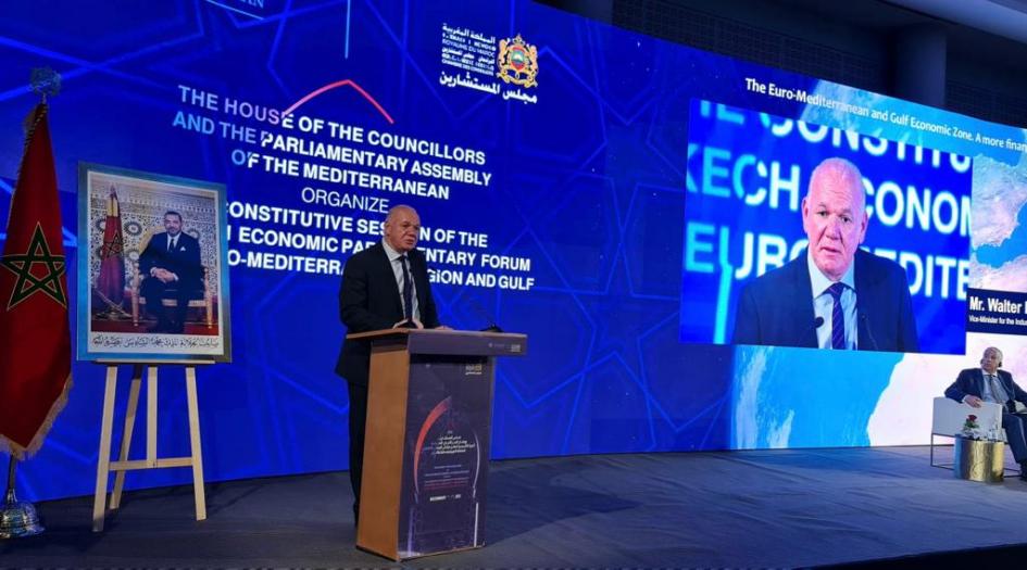 Verri expuso en el Foro Económico Euromediterráneo y de la Región del Golfo Verri habla desde un atril; a su lado, una pantalla con su cara; del otro, una foto de una autoridad