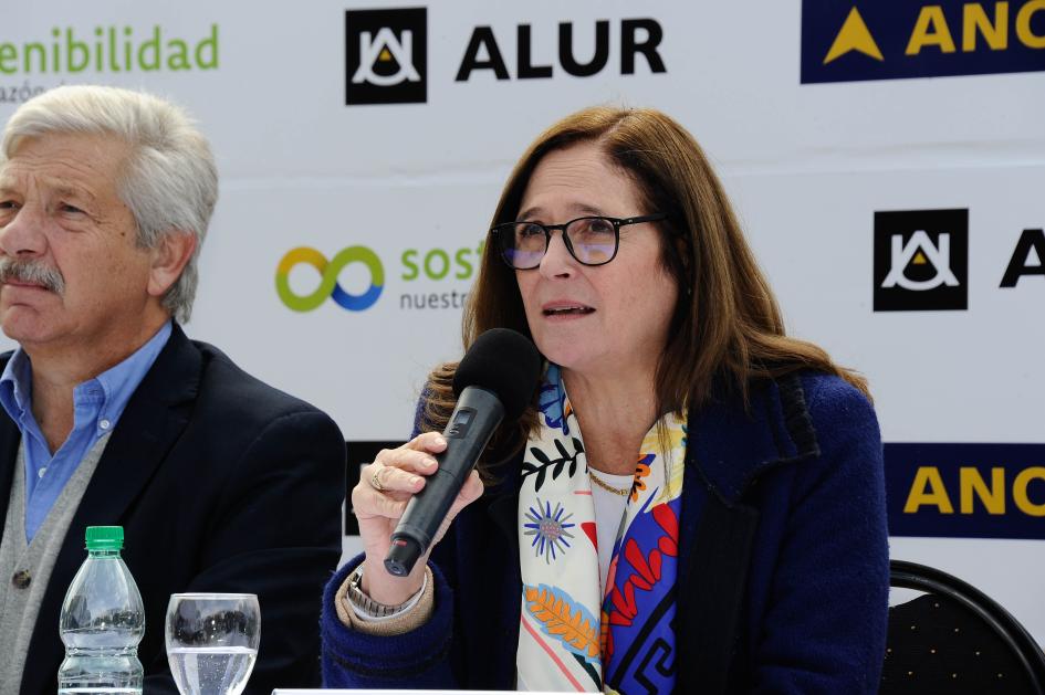 Ministra Elisa Facio Ministra Facio habla, junto a un hombre, en la mesa de autoridades; detrás, banner de ALUR