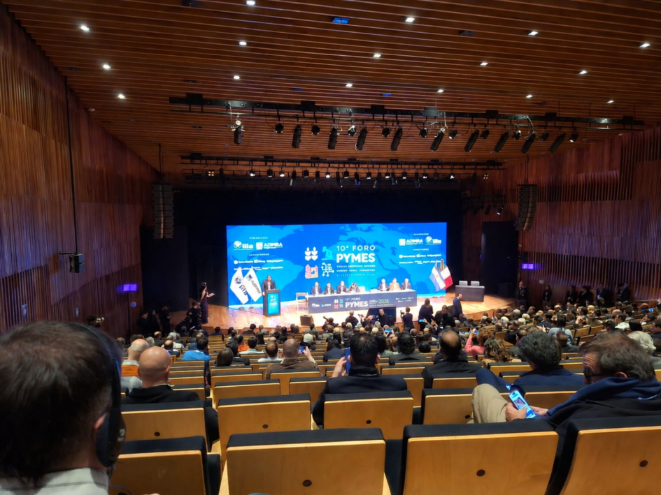 Panel del 10.° Foro Pymes Italia-América Latina Personas en un escenario; detrás, pantalla; más cerca y de espaldas, público
