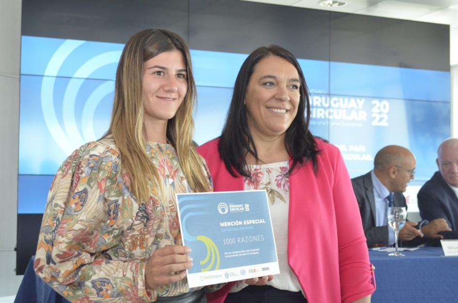 Mención en categoría Mipymes: 1000 razones Sánchez, junto a una mujer que sostiene el diploma; detrás, una gran pantalla, Albaladejo y Verri