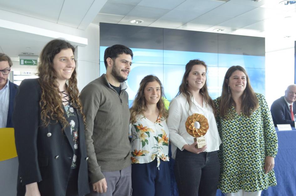 Camaño está junto a tres jovenes mujeres (una sostiene el premio) y un varón