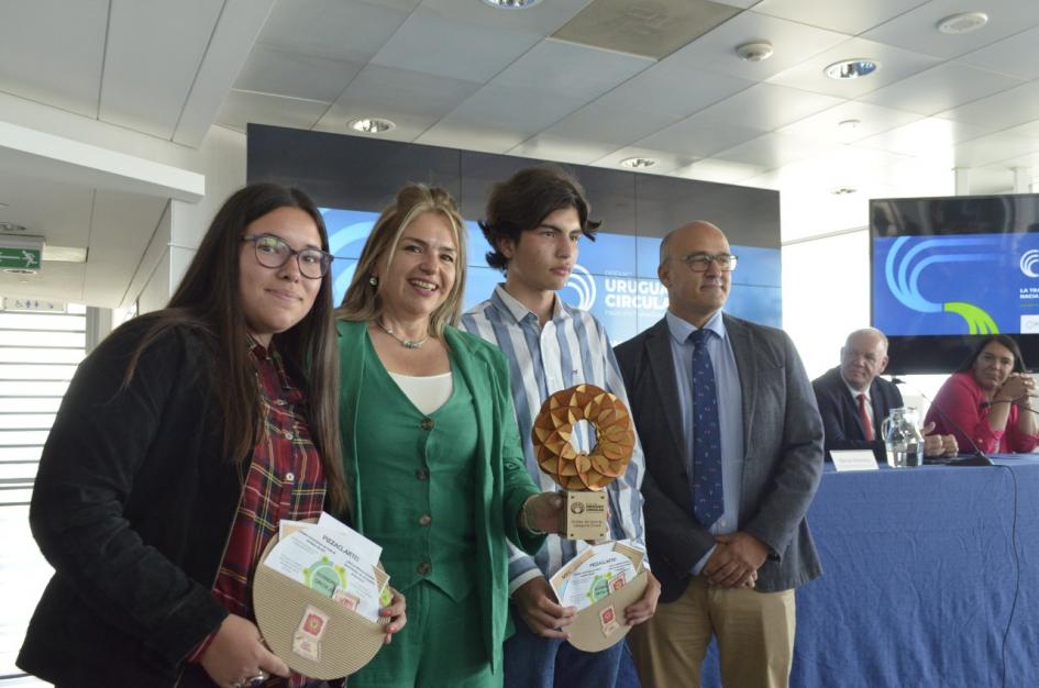 Premio en categoría Clubes de ciencia (Chajá): Escuela Agraria de Artigas Albaladejo junto a dos adolescentes (un chico y una chica; sostienen carpetas) y una mujer