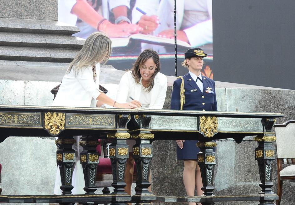 Asunción del cargo de la ministra Fernanda Cardona Ministra Cardona firma junto a una mujer; detrás, una militar y una pantalla