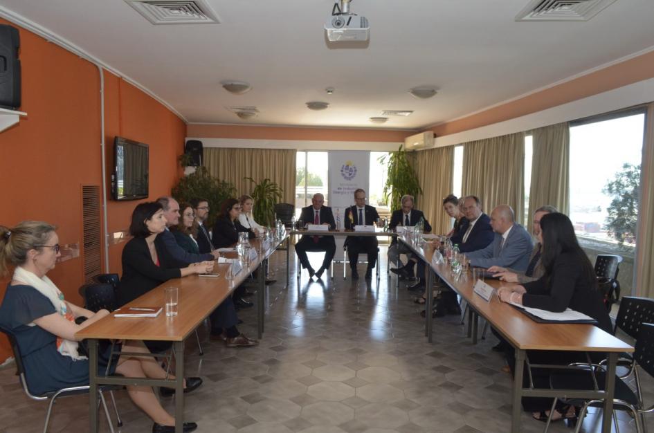 Participantes de la firma del memorando de entendimiento Participantes de la firma, sentados en mesas que forman un rectánculo; en dos paredes hay ventanas