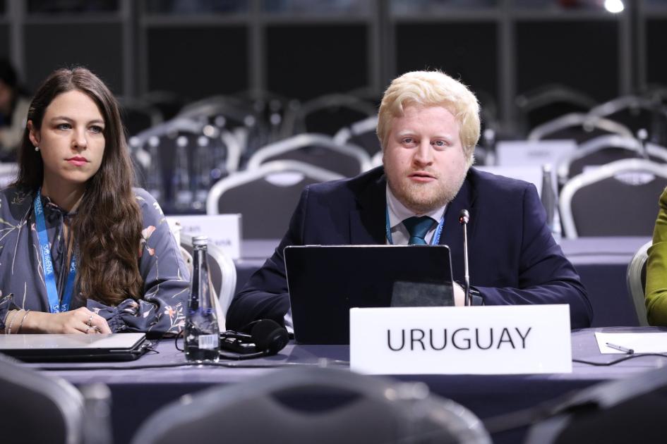 Director Christian Nieves representó a Uruguay en la asamblea de IRENA Director Nieves, junto a una mujer, habla en una mesa que tiene un cartel de Uruguay