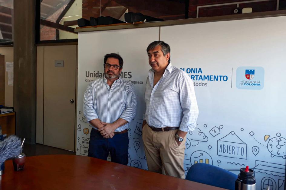Visita a la Unidad Pyme Maciel y otro hombre posan frente a un gran banner; frente a ellos hay una mesa