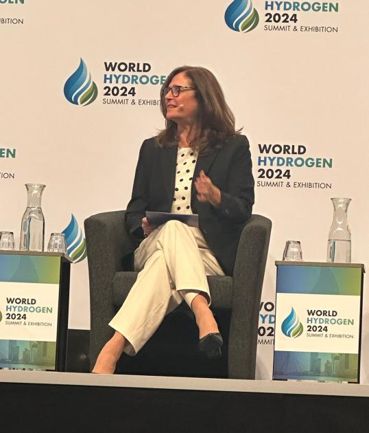 La ministra expuso al mundo acerca de la postura uruguaya sobre el hidrógeno verde y sus derivados La ministra Facio, sentada en un sillón; detrás, banner del evento