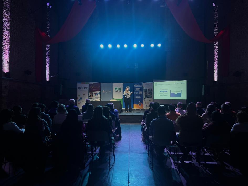 Taller Más Comercio de Uruguay XXI Sala con personas y la luz apagada; al fondo, hay una pantalla encendida