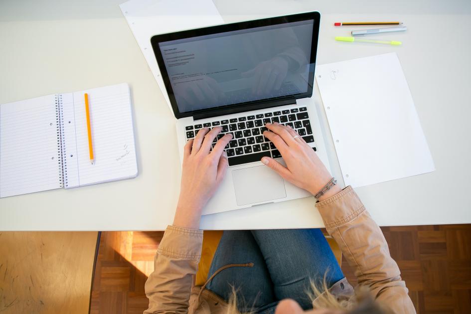 Dinamige comunica que un trámite en línea no estará disponible hasta nuevo aviso Persona escribe en una computadora, sobre una mesa