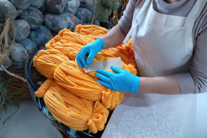 Manos con guantes celestes sobre pila de lanas naranjas
