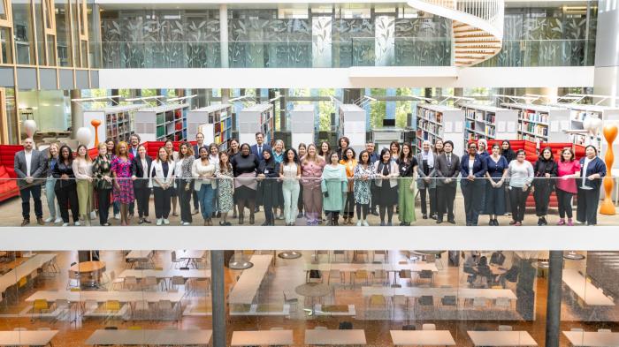 Participantes del simposio Numeroso grupo de participantes, de pie; debajo, salón vacío con sillas y mesas