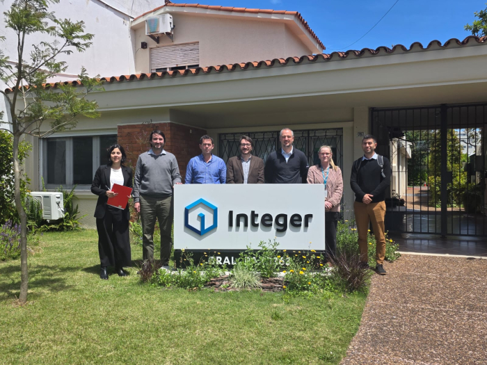 Personas de pie en un jardín, detrás de un cartel de la empresa